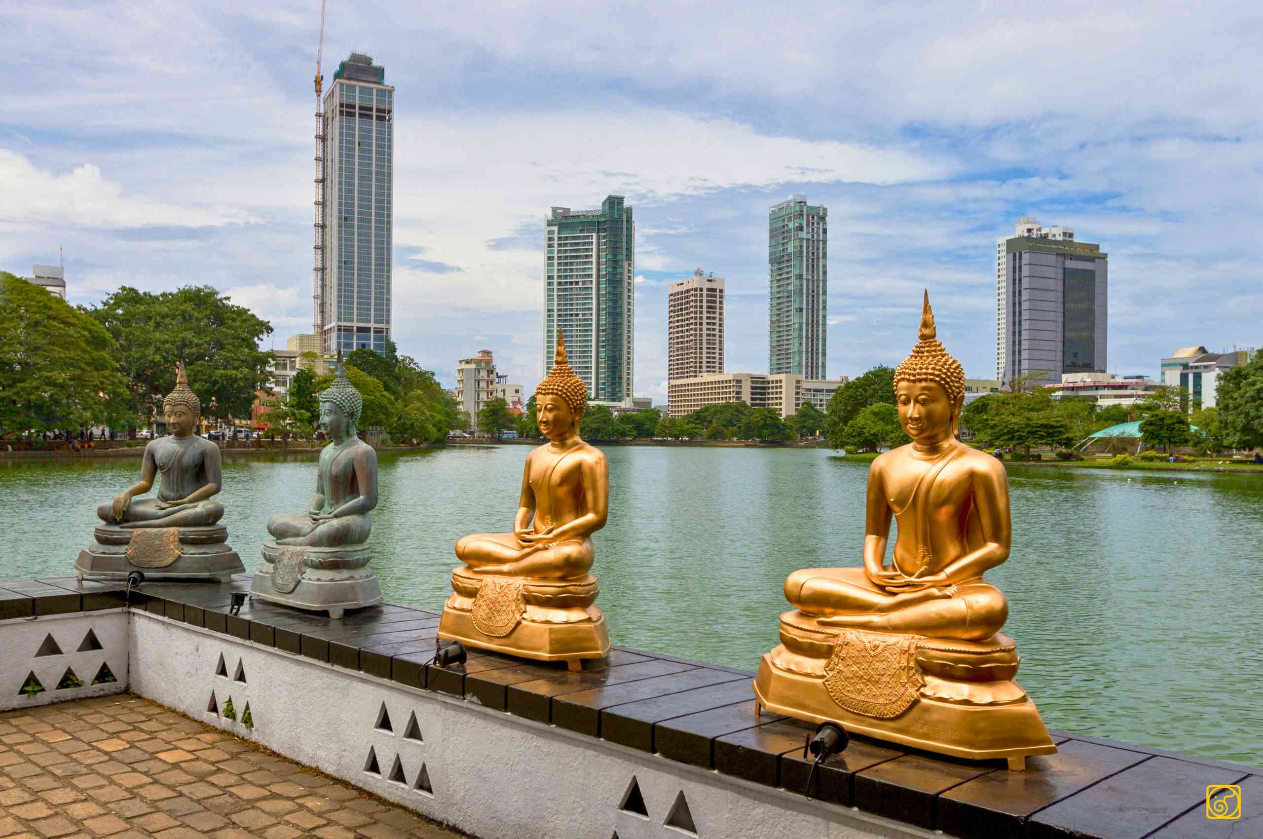 Golden Buddha statues at Gangaramaya Temple overlooking Beira Lake and the Colombo skyline
